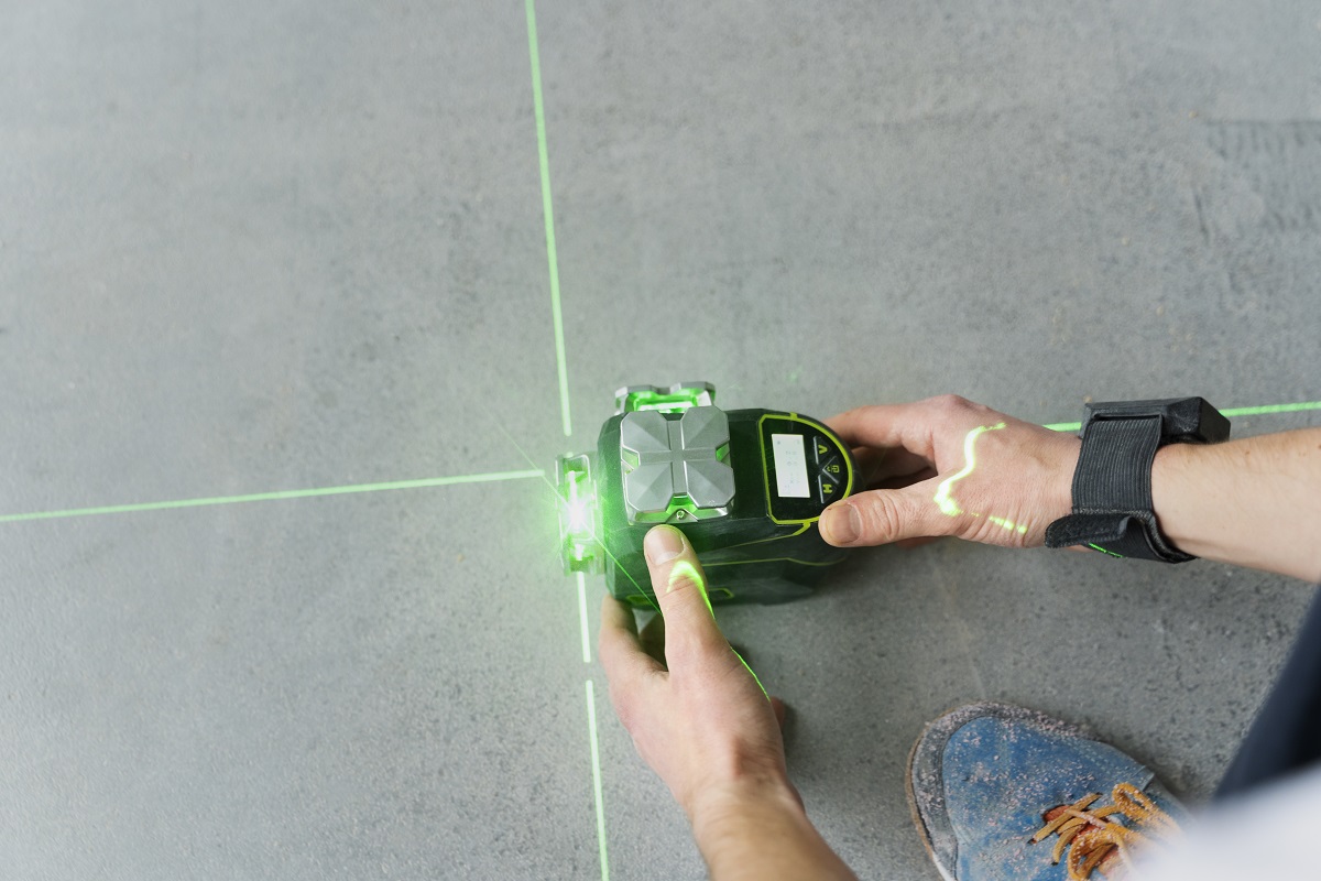 човек, който използва лазерен нивелир на 360 градуса huepar със зелени линиии на земята