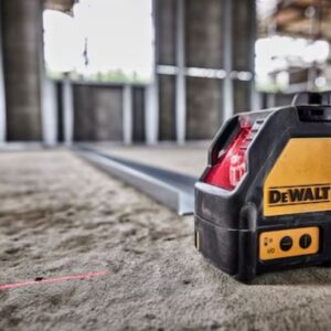 Лазерен нивелир DeWALT DW088K-XJ, поставен на пода, с ярко прожектирани червени линии, показващи неговата ефективност и точност.